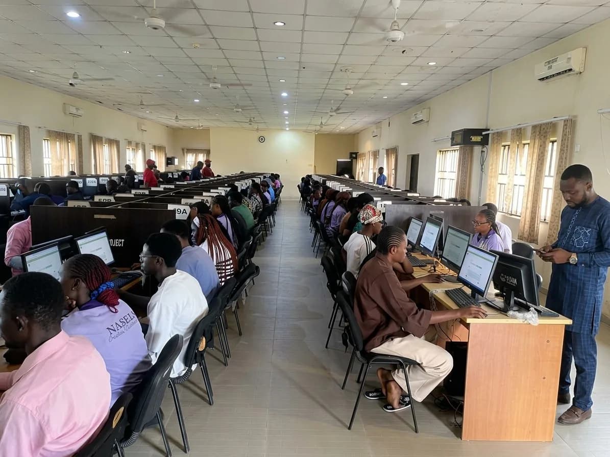 Students writing the Second Semester Examinations on computers in a University examination hall, with an invigilator standing by
